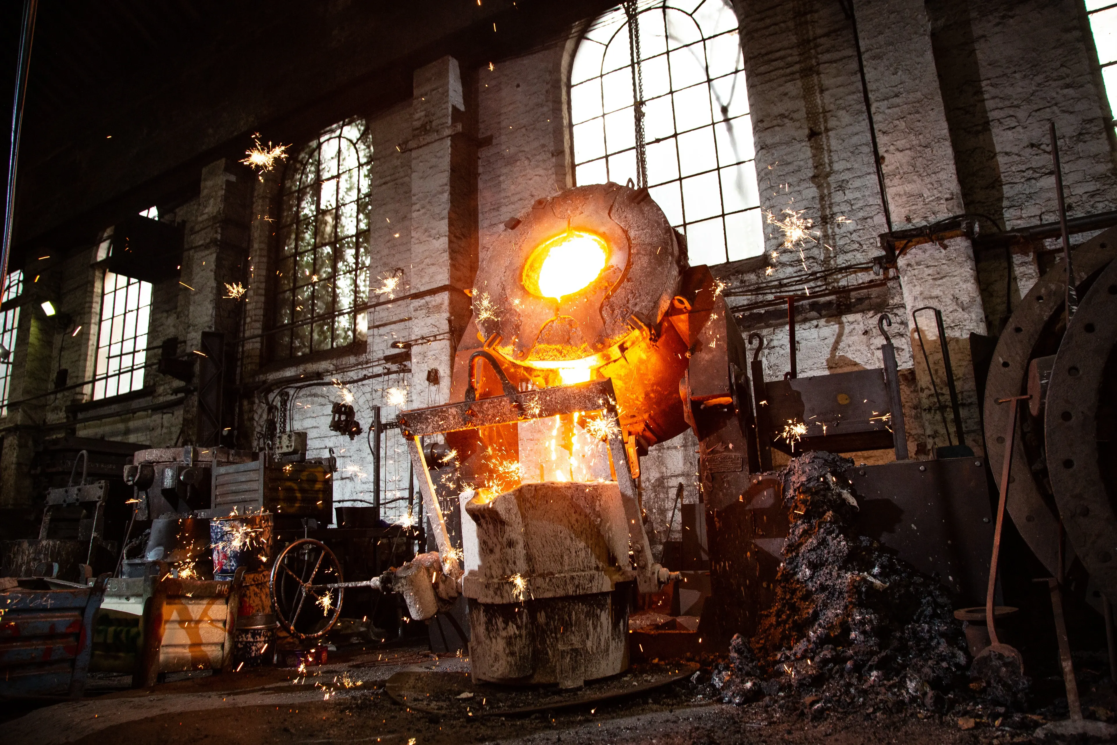 A crucible of molten bronze pouring into a bell mould in the casting hall at John Taylor and Co, sparks flying under tall arched windows