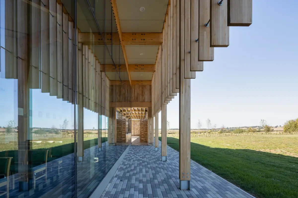 A glazed cloister running the length of the building, timber fins to one side and open countryside to the other