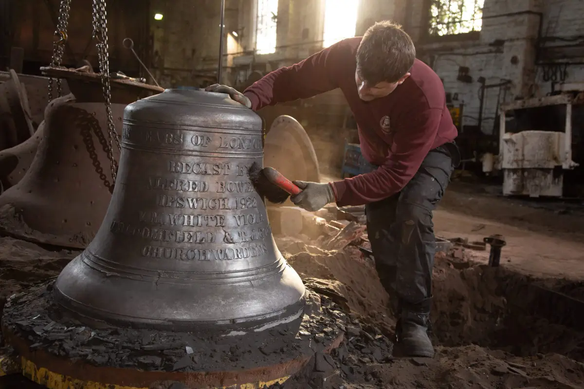 A founder brushing a recast bell hung on chains, its inscription naming Alfred Bowell of Ipswich and the churchwardens