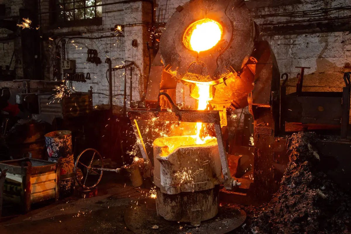 Molten bronze running from a tilting furnace into a ladle, sparks thrown across the casting hall