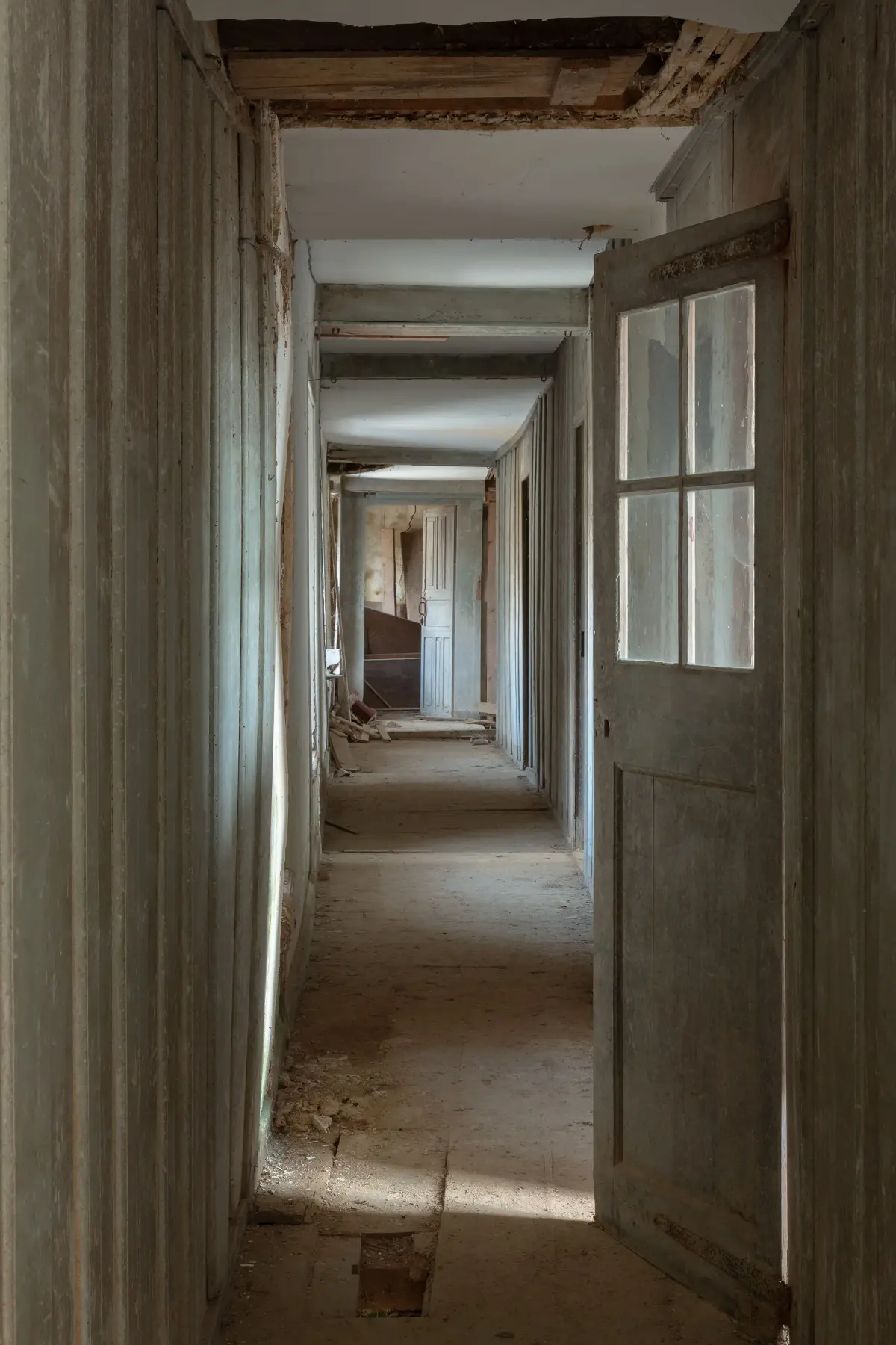 A panelled corridor running the length of the house, doors standing open along it and rubble on the boards