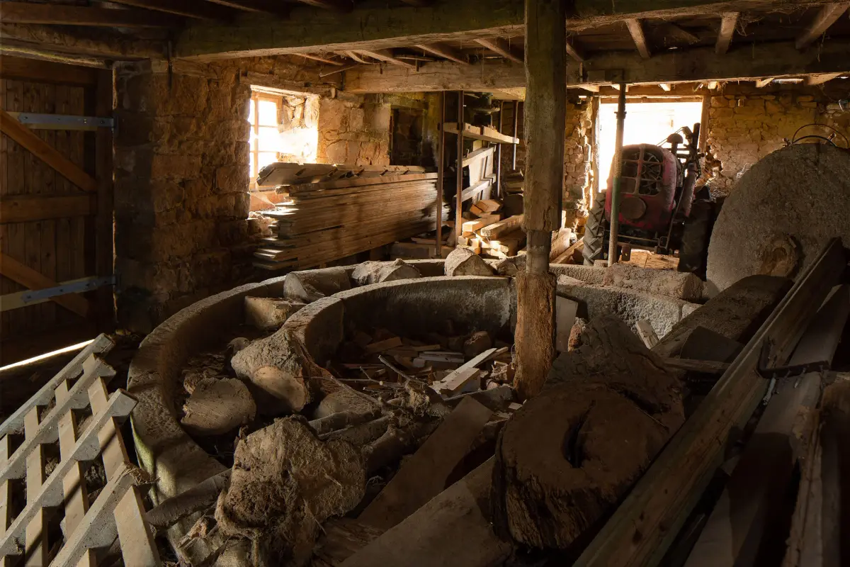 A granite apple crusher, its circular trough and runner stone, standing in a barn with a tractor beyond