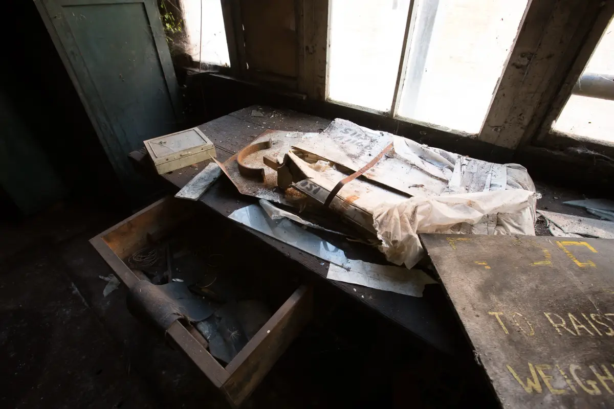 A bundle still wrapped and strapped on a workbench by a window, a stencilled instruction to raise the weight on the beam beyond
