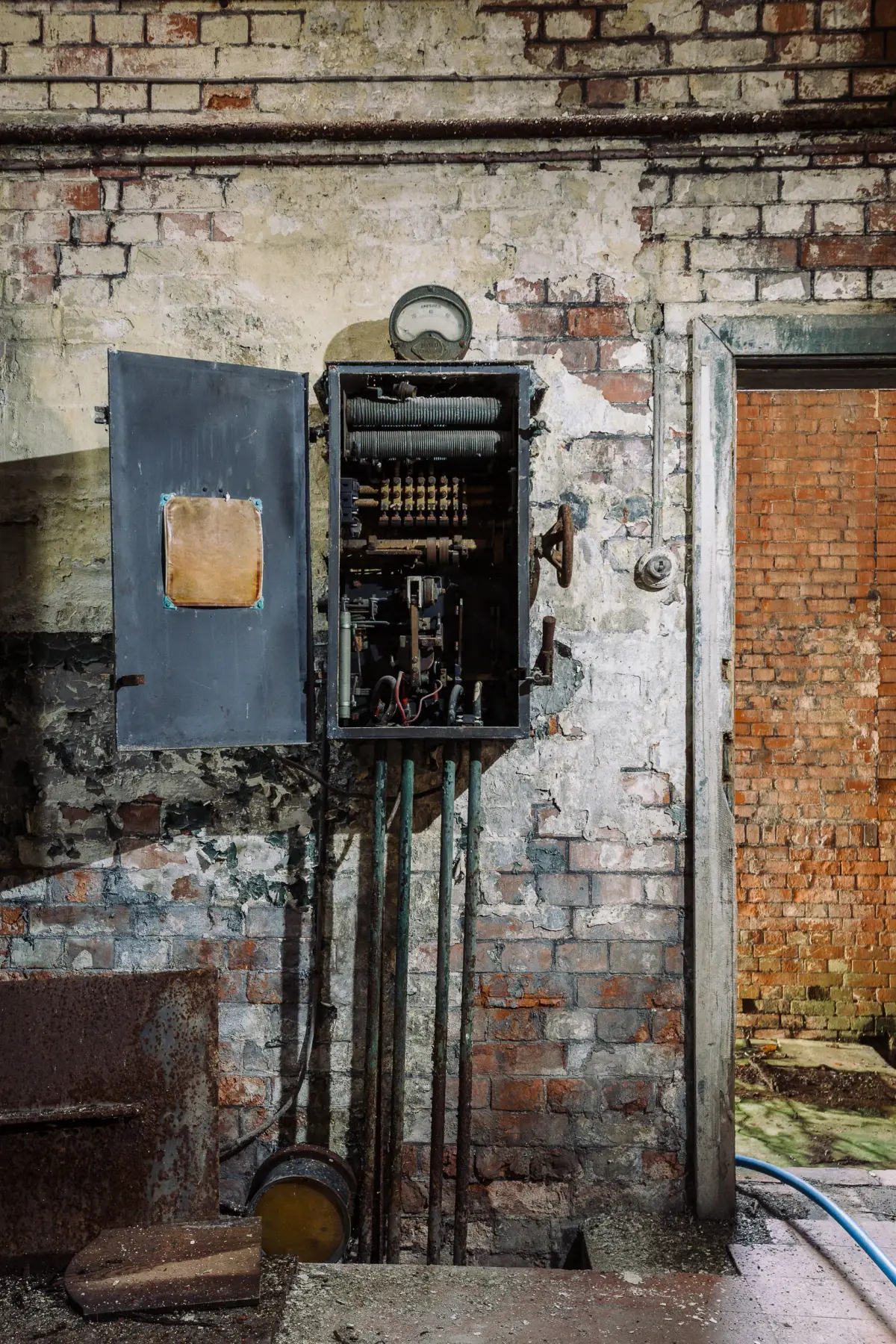 An open switchgear cabinet on a brick wall, its resistance coils and contacts exposed, conduits dropping to the floor