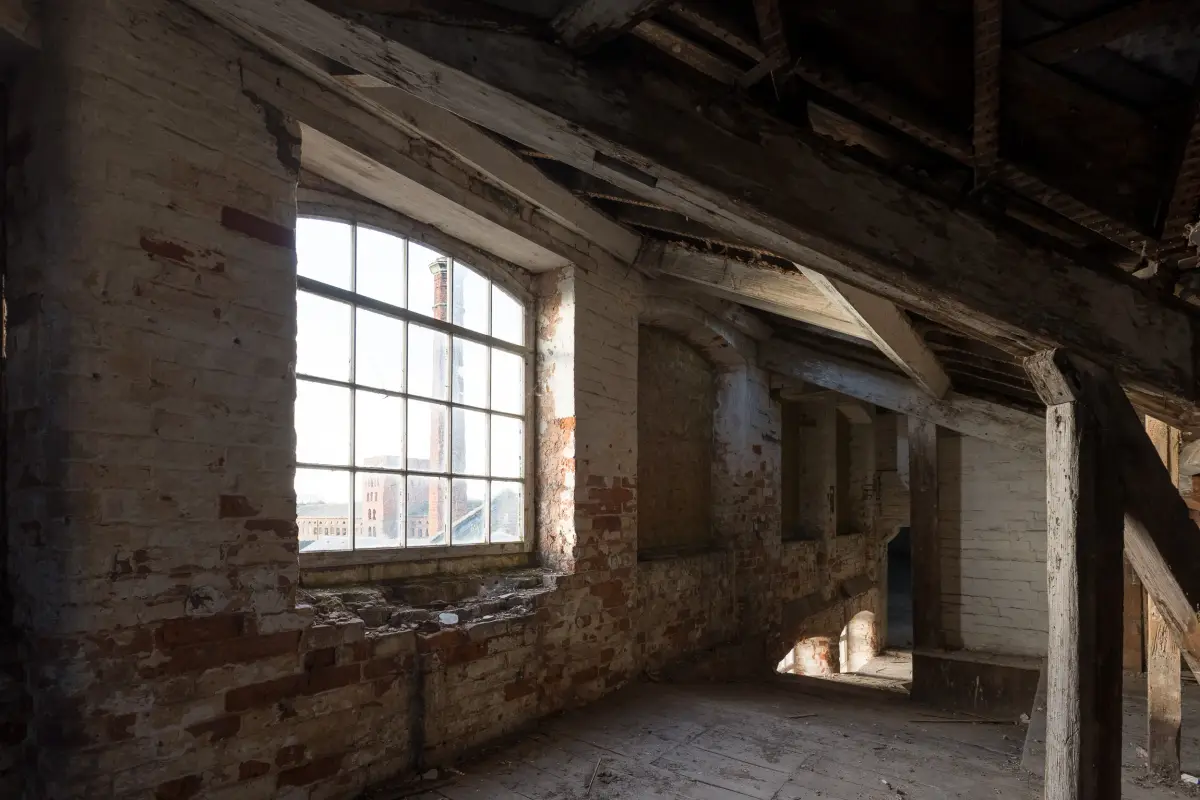 A top floor room with an arched window looking across to the mill chimney, roof timbers open above