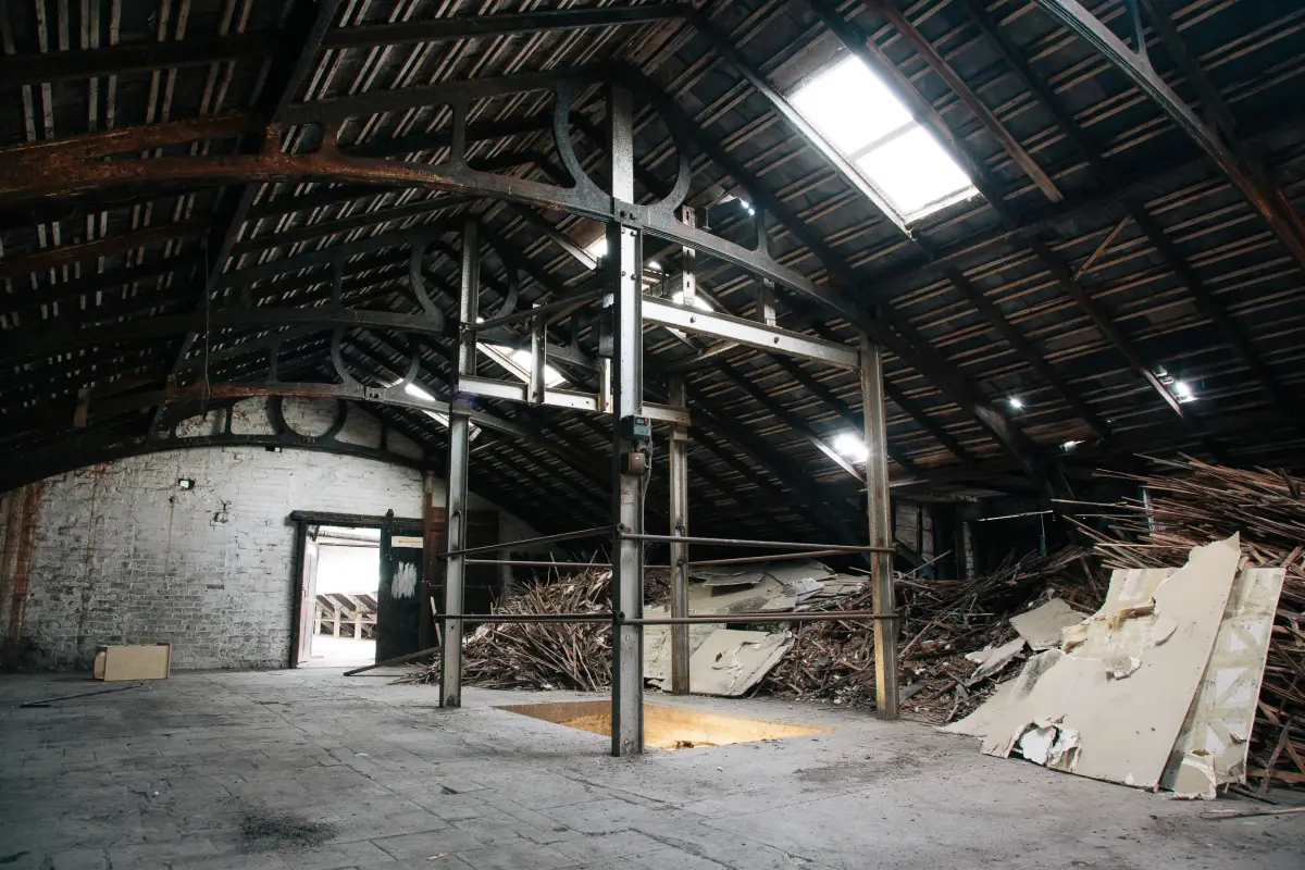 A roof space carried on cast iron arched trusses, daylight from a skylight, laths and broken board heaped to one side