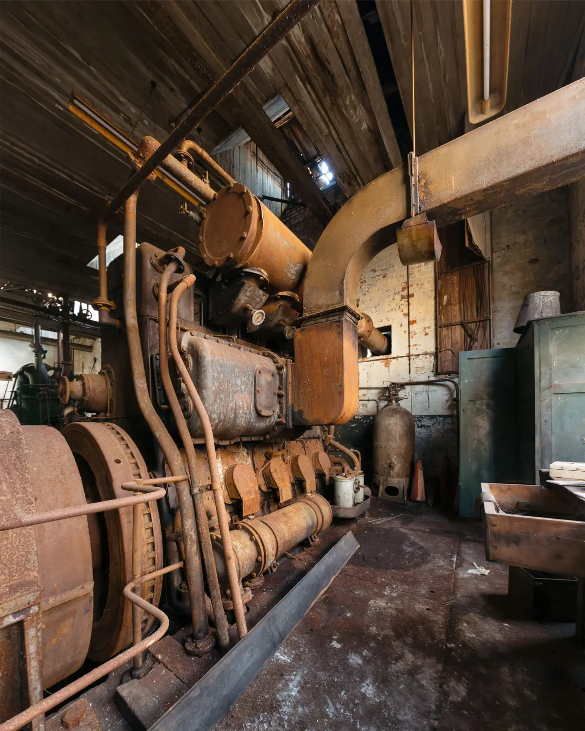 A rusted engine and its pipework filling the width of an engine house, flywheel to the left